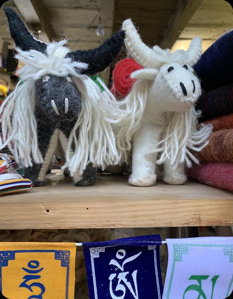 Handcrafted felt animal figurines on a shelf with prayer flags