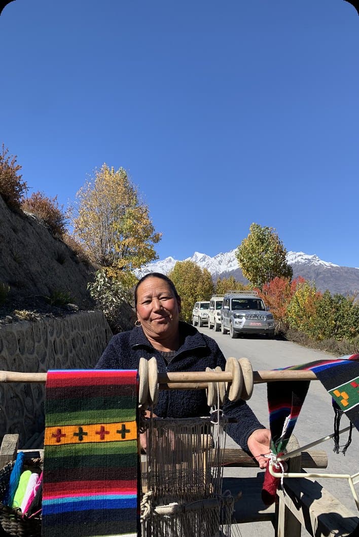 Artisan weaving textiles beside a mountain road
