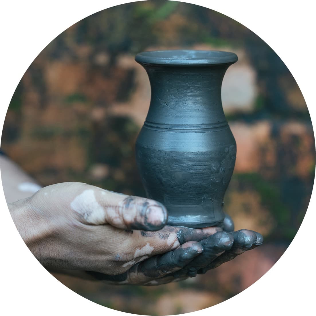 Hands covered in clay holding a ceramic vase