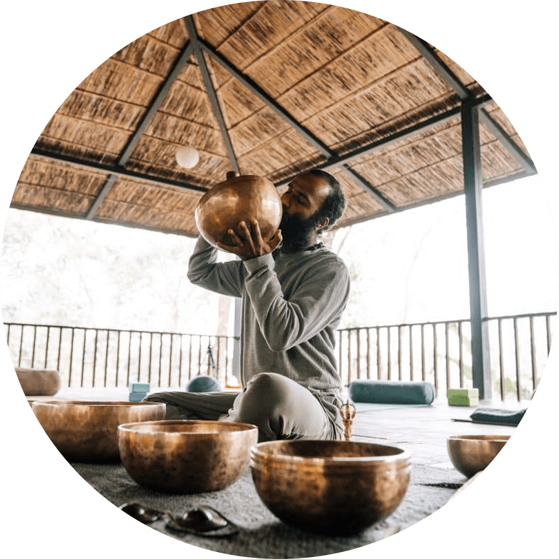 Practitioner with singing bowls under a thatched pavilion at Kasara